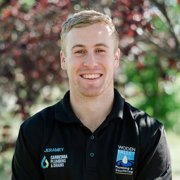 Andrew, a professional plumber from Canberra Plumbing & Drains, smiling outdoors in a black uniform.